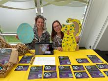 Two women in leopard onesies sit behind a table covered in flyers for Funcon 1