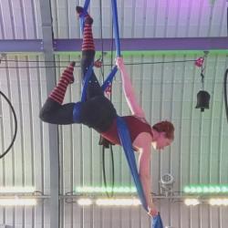 Emma hanging upside down in the air, suspended by lengths of blue fabric.